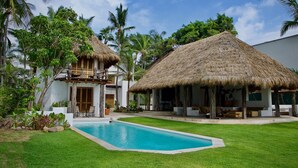 A resort with a swimming pool, thatched-roof structures, and lush greenery.
