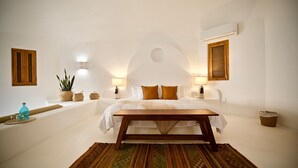 A bedroom with a bed, bedside tables, a wooden bench, a patterned rug, and wall-mounted lamps.