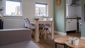 A modern living room with a sofa, dining table with chairs, and a kitchen area with cabinets and a sink.