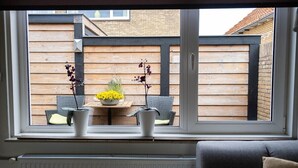 A view from a window with a wooden fence, a table with yellow flowers, and two potted plants.