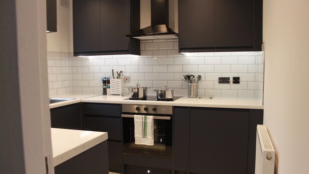 Una cocina moderna con armarios oscuros, horno de acero inoxidable y salpicadero de azulejos blancos.