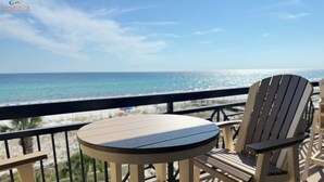A deck with a round table and two Adirondack chairs, overlooking a beach and the ocean. - Azure 404 | 4BD  | Gulf Views + Covered Balcony | FREE Beach Setup (Fort Walton Beach)