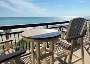 Una terraza con una mesa redonda y dos sillas Adirondack, con vistas a la playa y al océano.
