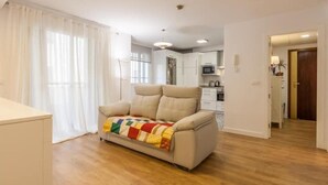 Un salón amplio con un sofá beige, una manta colorida y suelo de madera.