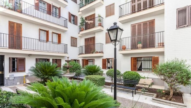 Un edificio residencial de varios pisos con balcones, una fuente central y abundante vegetación.