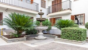 Un patio central con una fuente, rodeado de setos cuidados y palmeras.
