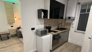A modern kitchen with a built-in oven, microwave, and sink. There is a small refrigerator and a wooden cabinet. - Charmant Appartement Joinvillais (Joinville-le-Pont)