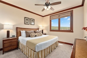 A hotel room with a bed, nightstands, a ceiling fan, a window with a view, and framed pictures on the wall.