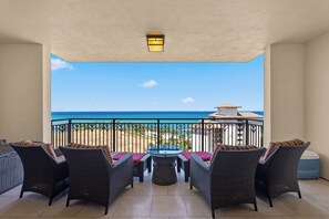 A balcony with wicker furniture, a glass table, and a view of the ocean.
