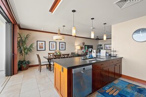 A modern kitchen with a central island, pendant lighting, and a dining area with chairs and a table. - Ko Olina Beach Villas O1404 by Gather: Penthouse Villa w/ Lagoon & Ocean Views (Kapolei)