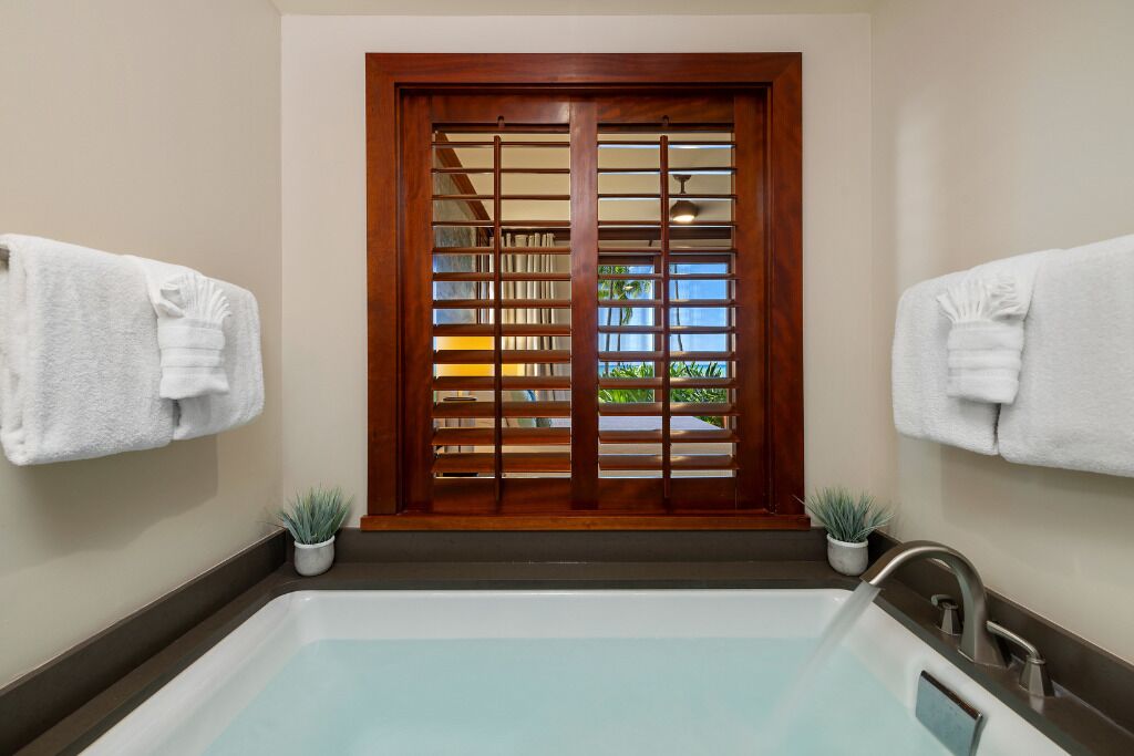 Ein Badezimmer mit einer Badewanne, zwei Handtüchern an Haken, einer Holztür mit Fenster und zwei Topfpflanzen.
