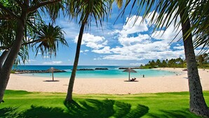 A beach with clear turquoise water, palm trees, and two thatched umbrellas.