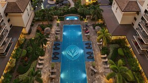 A rooftop pool with a central water feature, surrounded by lounge chairs and palm trees, with buildings on either side.