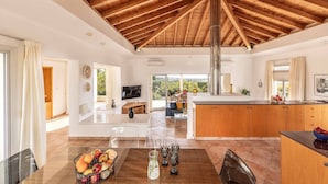 A spacious living area with a high wooden ceiling, a kitchen with wooden cabinets, and a dining area with a glass table.