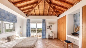 A bedroom with a wooden ceiling, a bed with a patterned bedspread, a desk, and a chair.