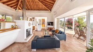 A spacious living area with a high wooden ceiling, a fireplace, and a large sliding glass door leading to an outdoor patio.