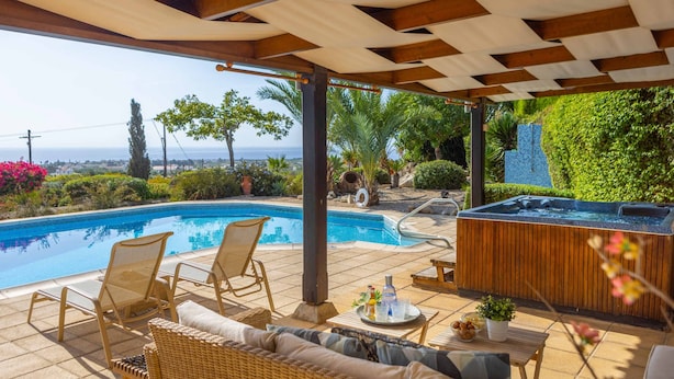 A poolside area with a hot tub, lounge chairs, and a view of the sea.
