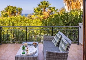 Relax on the balcony with a wicker sofa and enjoy the sea view surrounded by lush greenery and palm trees.