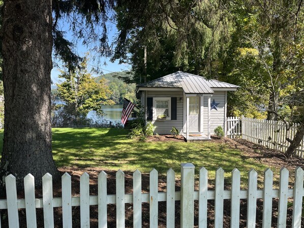A small cabin with a white picket fence, a mailbox, and a flagpole with an American flag.