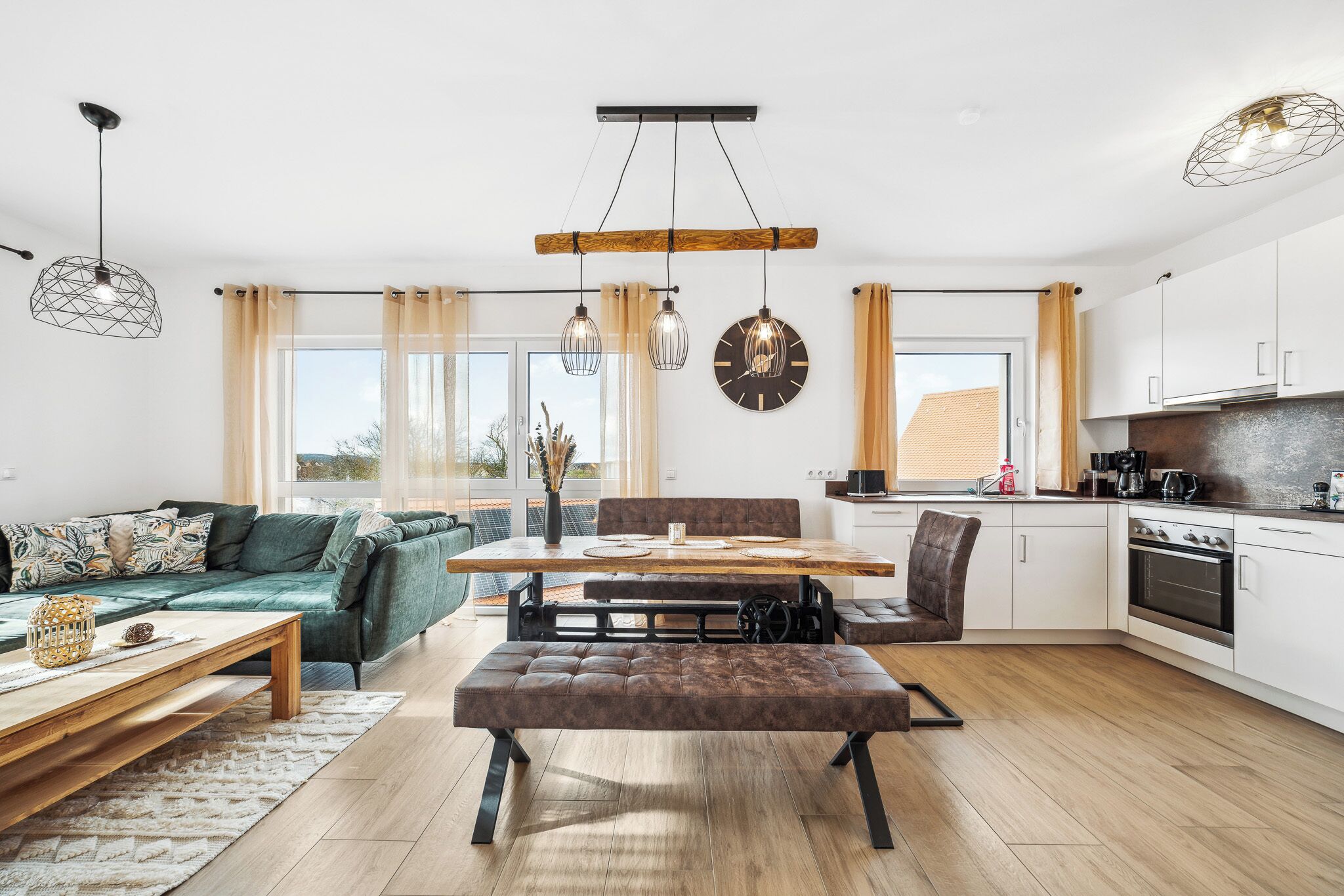 Een moderne woonkamer met een bank, eettafel, een bankje en een keuken met kasten en apparatuur.