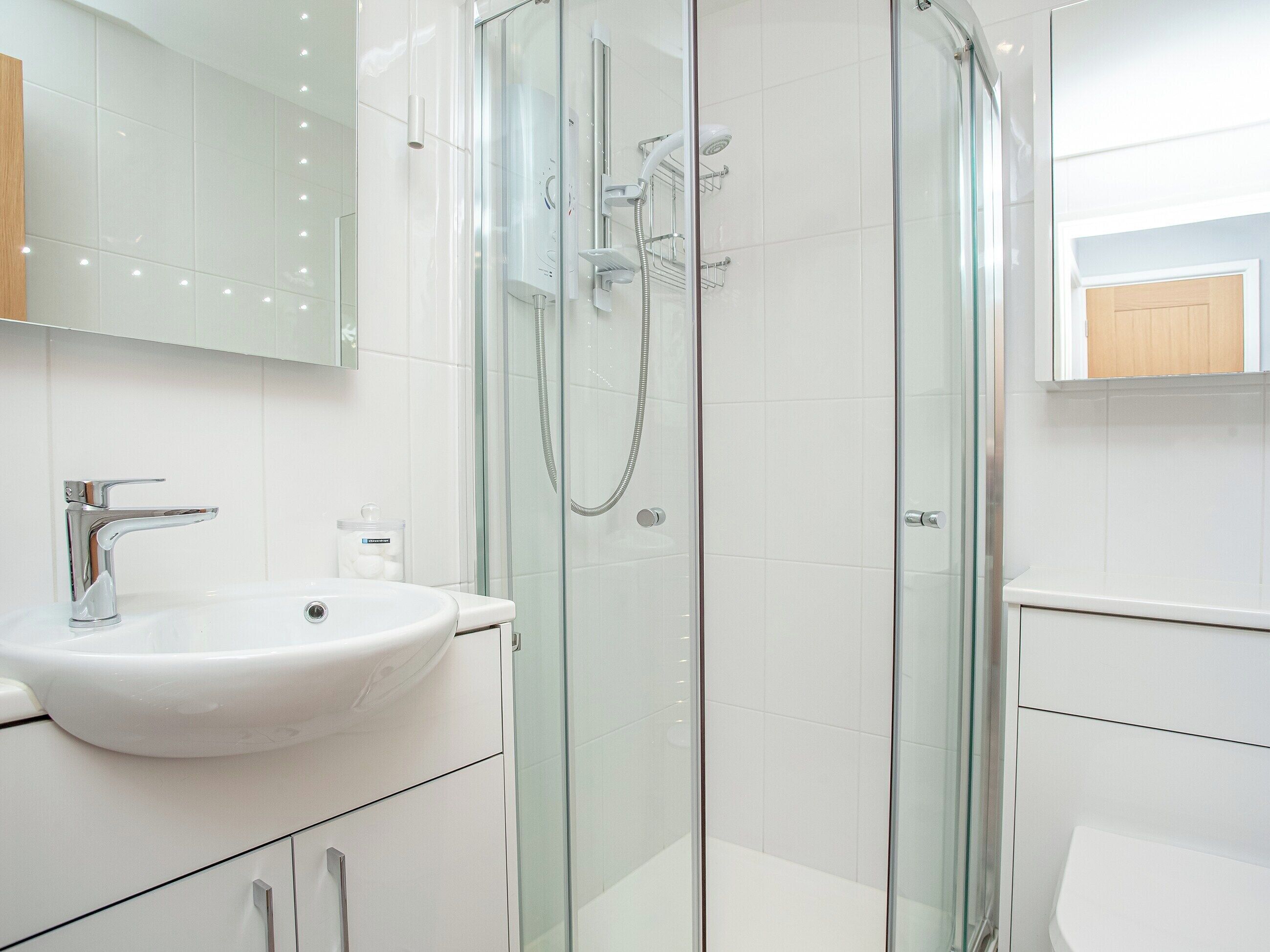 Un baño moderno con ducha de vidrio, lavamanos blanco y espejo sobre el lavamanos.