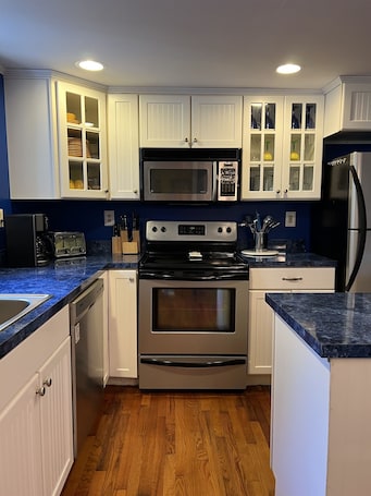 A kitchen with white cabinets, a stainless steel microwave, a stove, and a refrigerator.