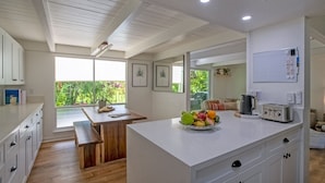 A modern kitchen with white cabinets, a wooden dining table, and a fruit bowl on the counter.