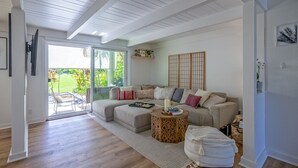 A living room with a beige sectional sofa, a wooden coffee table, and a view of a garden through glass doors.