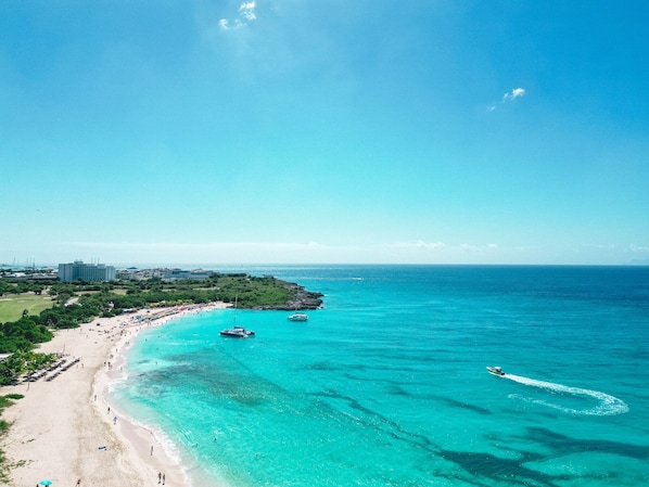 A beach with clear turquoise waters, a boat, and a distant building.