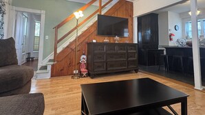 Un salón con una escalera de madera, un televisor montado en la pared, un aparador de madera oscura y una mesa de centro negra.