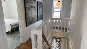 Una escalera con barandilla blanca, piso de madera y una cama con cubrecama blanco en la habitación contigua.