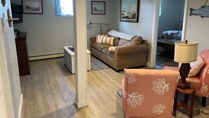 A living room with a brown sofa, a small table, and a lamp. There is a door leading to another room.