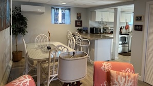 A compact kitchen with white cabinets, a microwave, and a stove. There is a dining area with a table and chairs, and a small island with a lamp.