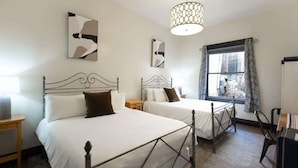 A hotel room with two beds, a large window with curtains, a hanging light fixture, and abstract wall art. - Deluxe Room at The Block (Bisbee)