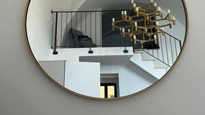 Un espejo redondo con marco dorado que refleja una escalera, una lámpara de araña y un zapatero.
