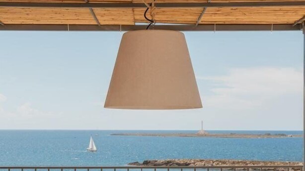 Terraza con mesa y sillas, con vista al mar y un velero, junto a un faro.