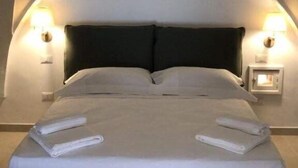 Una cama con cabecera oscura, dos lámparas de noche y una lámpara fijada a la pared.