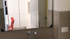 Un baño con un lavabo blanco, un espejo encima y una silla roja al fondo.