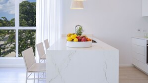 A modern kitchen with a marble island, white cabinetry, and a large window with a view of trees. - Palm Grove Villas & Hotel (Mount Standfast)