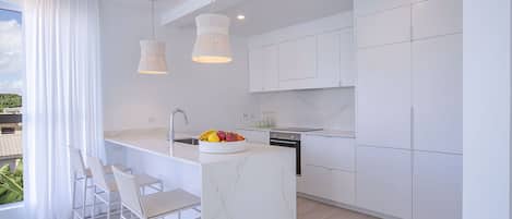 A modern kitchen with white cabinetry, a marble island, and pendant lighting.