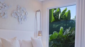 A bedroom with a large bed, a ceiling fan, a wall-mounted light, and a view of greenery through a window. - Palm Grove Villas & Hotel (Mount Standfast)