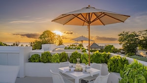 An outdoor patio with white furniture, a table set for dining, and a large umbrella providing shade. - Palm Grove Villas & Hotel (Mount Standfast)