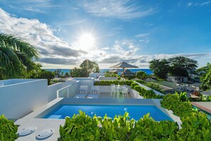 Zona de piscina en la azotea con vistas despejadas al océano, rodeada de exuberante vegetación y arquitectura moderna.