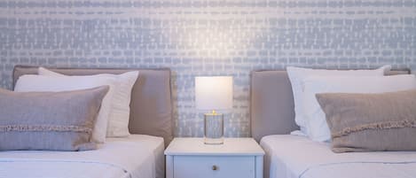 A hotel room with two beds, a nightstand with a lamp, and a patterned wall.
