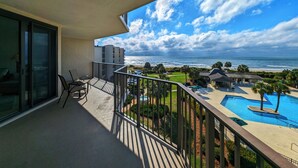 En balkon med udsigt over havet, en swimmingpool og en bygning i baggrunden.