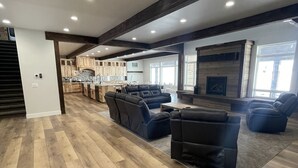 Un vaste espace de vie doté d’un plancher en bois, d’une cheminée et d’un coin repas avec des meubles de rangement en bois, et une cuisine en arrière-plan.