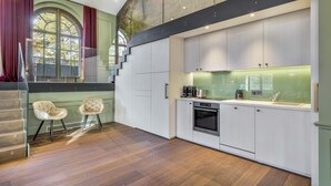 A modern kitchen with a built-in oven, a large window with curtains, and a staircase leading to an upper level. - Le Loft 150 m² vue rivière (Lyon)