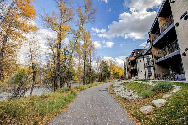 A pathway leading to a building with a modern architectural style, surrounded by autumn foliage and a body of water.