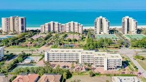 Een hoog hotelcomplex met meerdere gebouwen, een zwembad, tennisbanen en uitzicht op het strand.