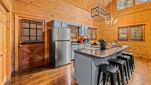 A wooden cabin interior with a kitchen featuring a refrigerator, bar stools, and a wooden ceiling.
